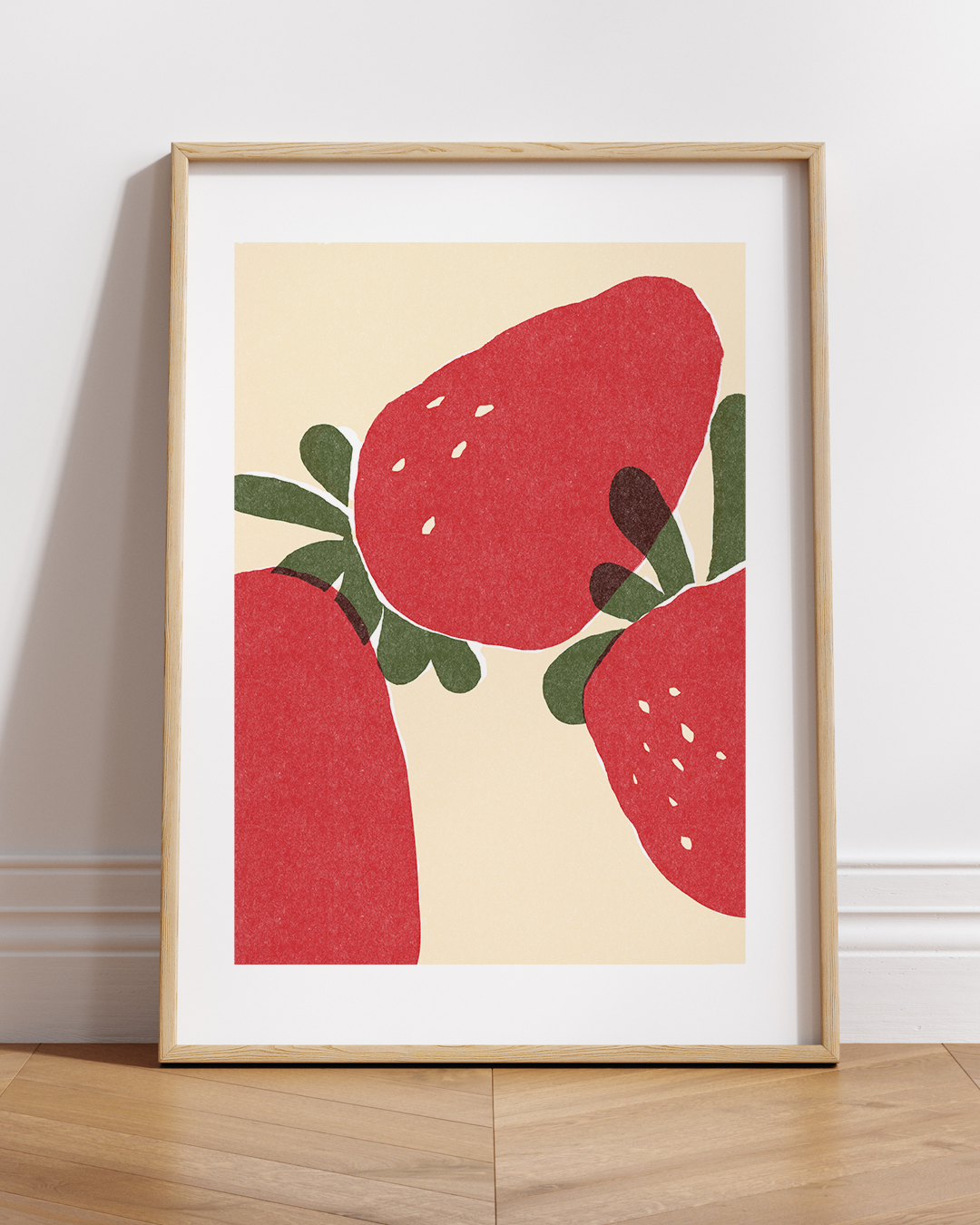 Strawberry artwork framed and placed on a wood shelf in a bright room