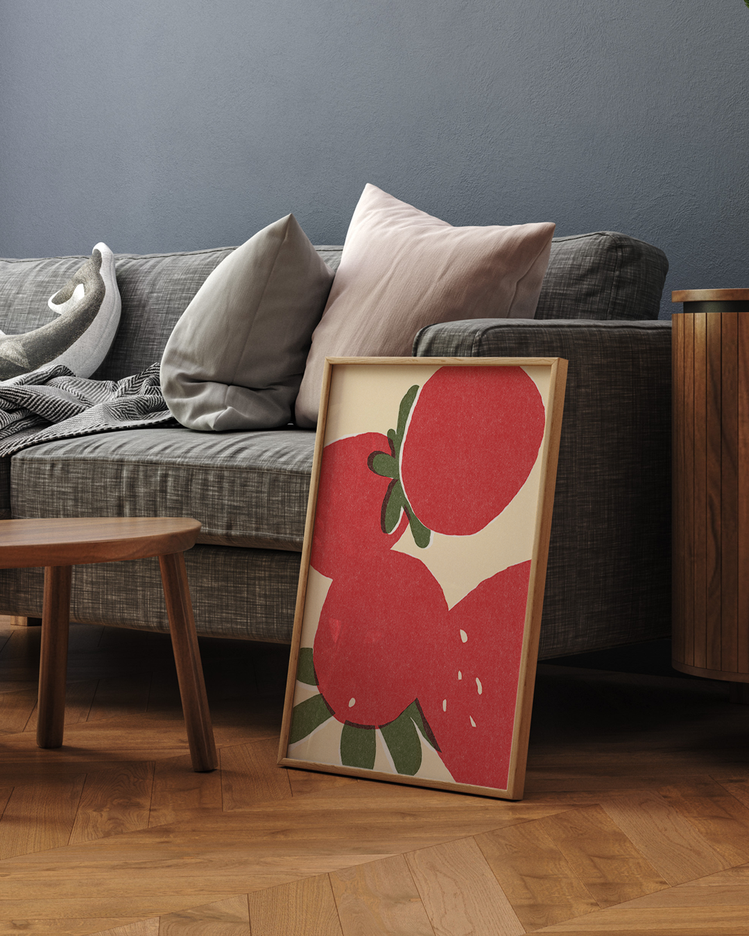 Strawberry Art Print resting on chair beside a grey couch in soft light